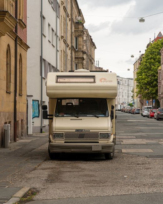 A man seated in the driver's seat of a white delivery van, with the driver's side door open, is holding a cardboard box in his hands during a home relocation process. The van is parked on a residentia